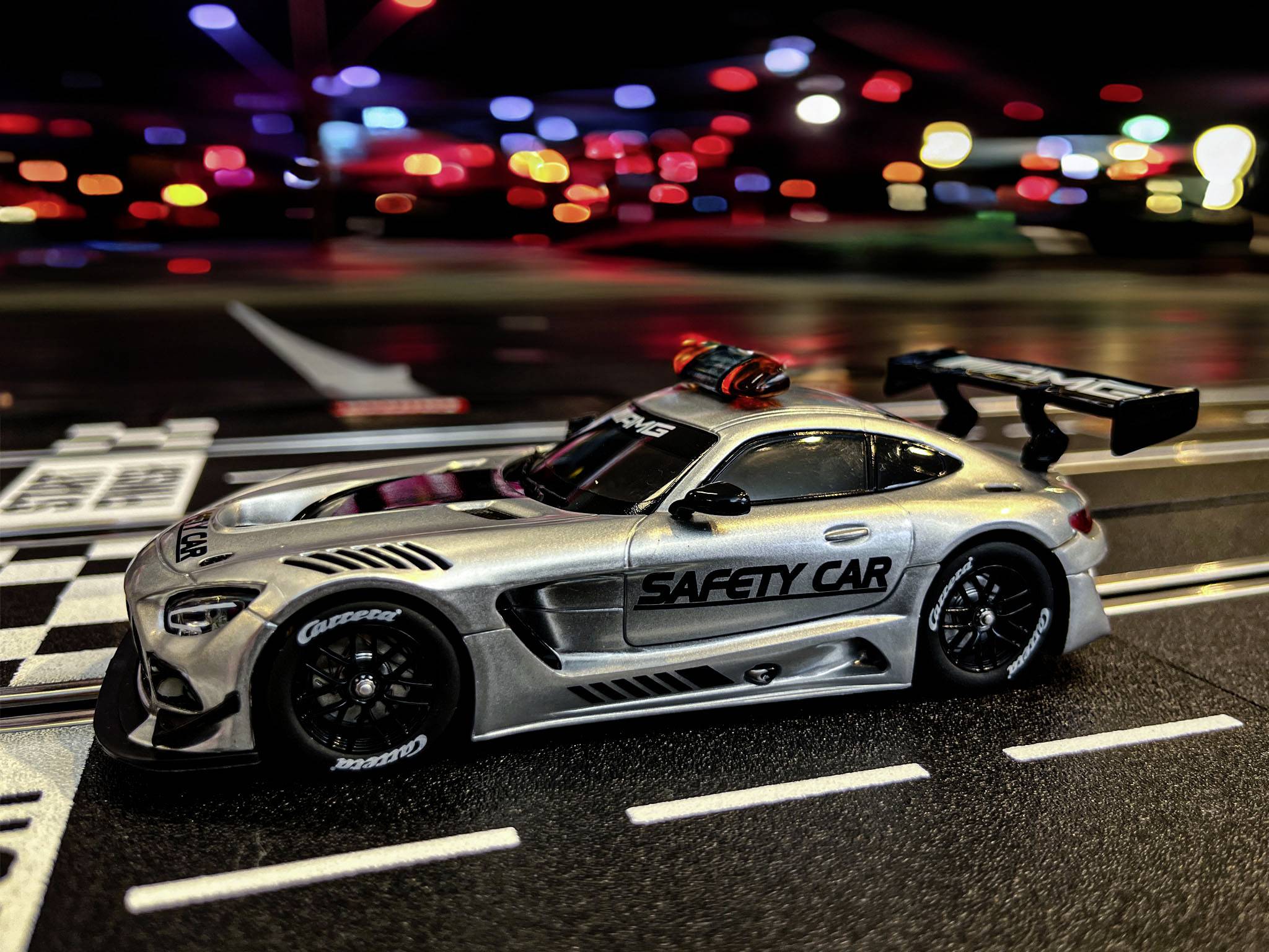 Toy safety car on a racing track with colourful lights in the background.