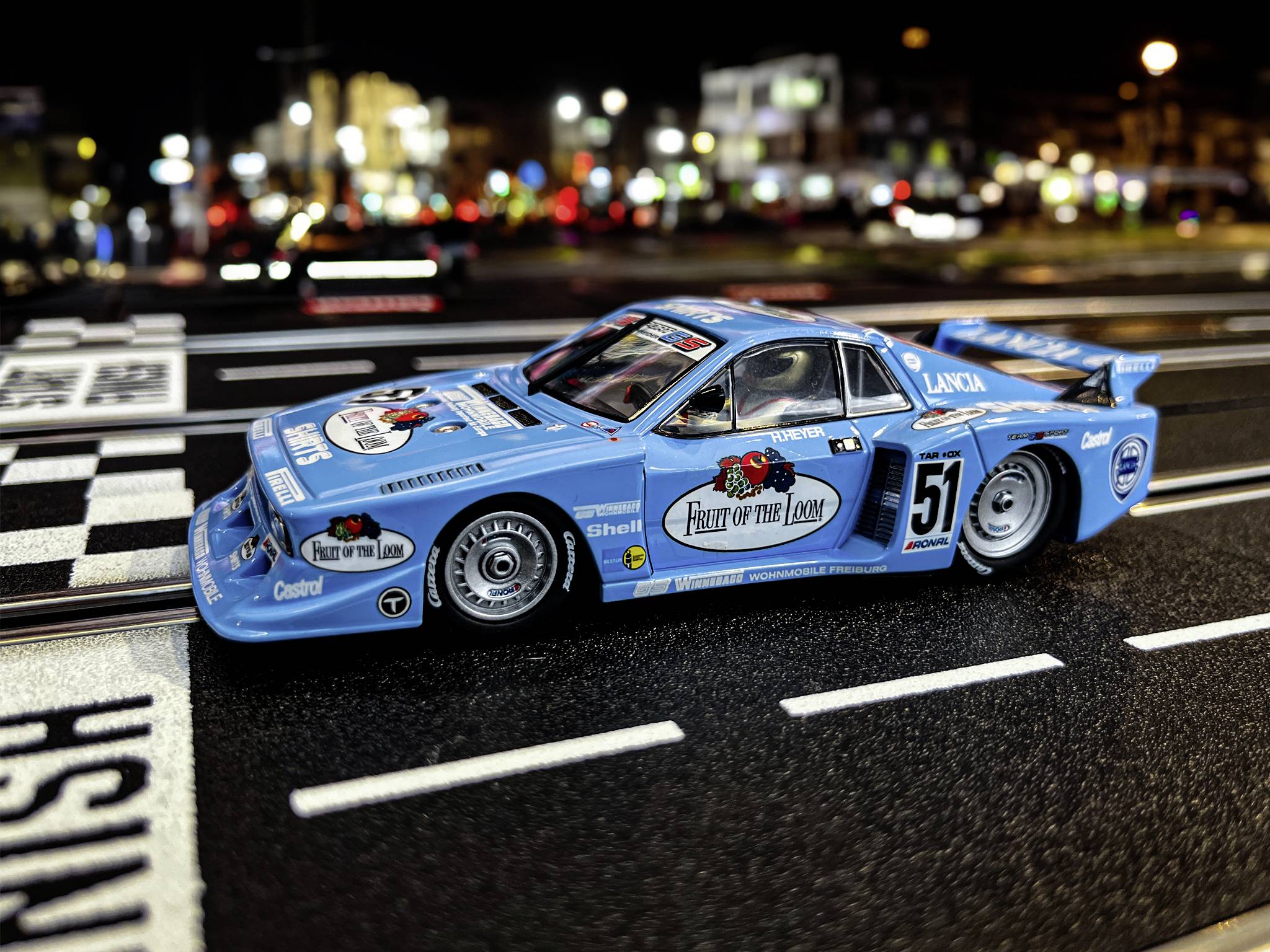 Blue toy racing car with 'Fruit of the Loom' written on the bonnet, standing on a race track.