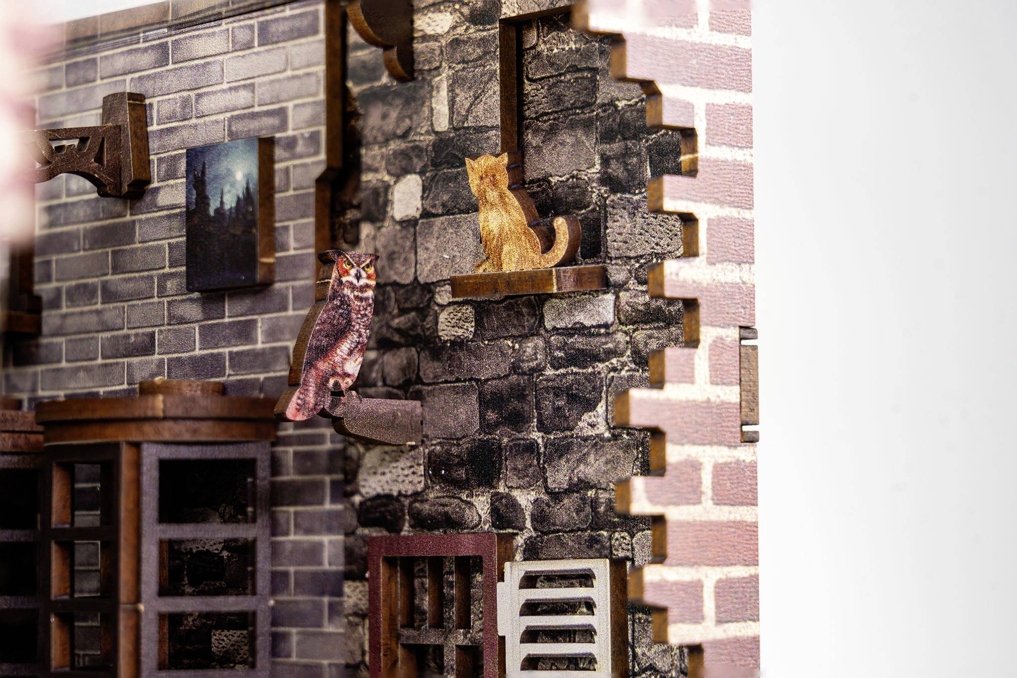 An owl and a cat are sitting on windowsills of a miniature building with brick masonry.
