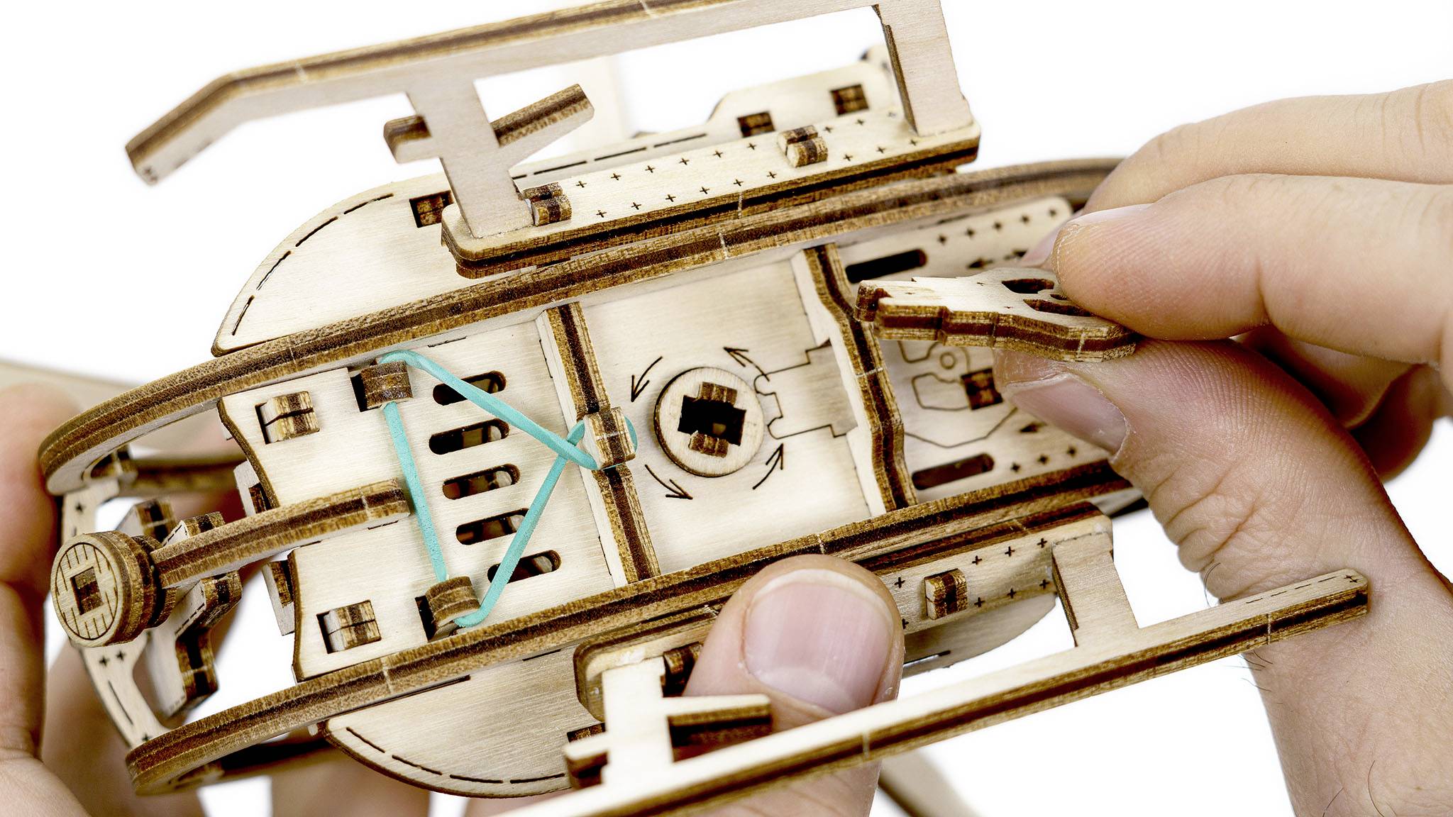 Hands are assembling a wooden model. A rubber band is visible, appearing to be part of a mechanical wooden puzzle.