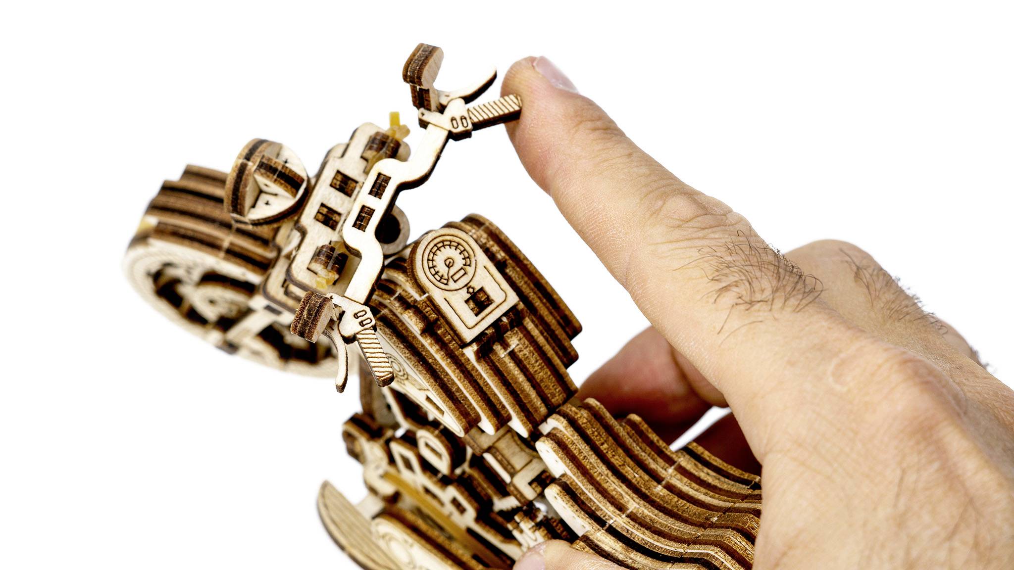 A finger is turning a wooden model kit. The intricate design reveals gears and structures that emphasise mechanical expertise.