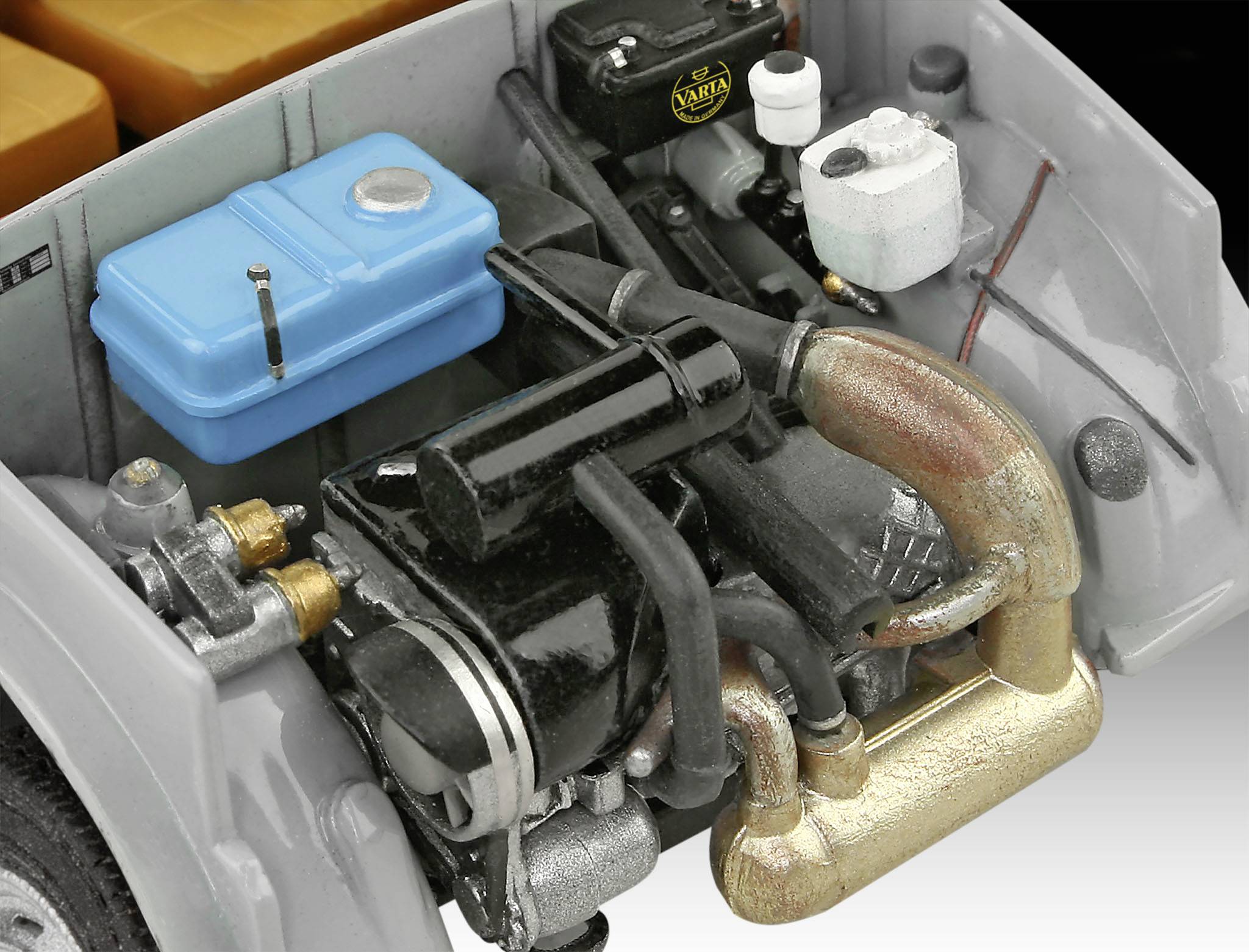A model car engine bay with coloured parts: a blue container, black and brass-coloured components, including pipes and hoses.