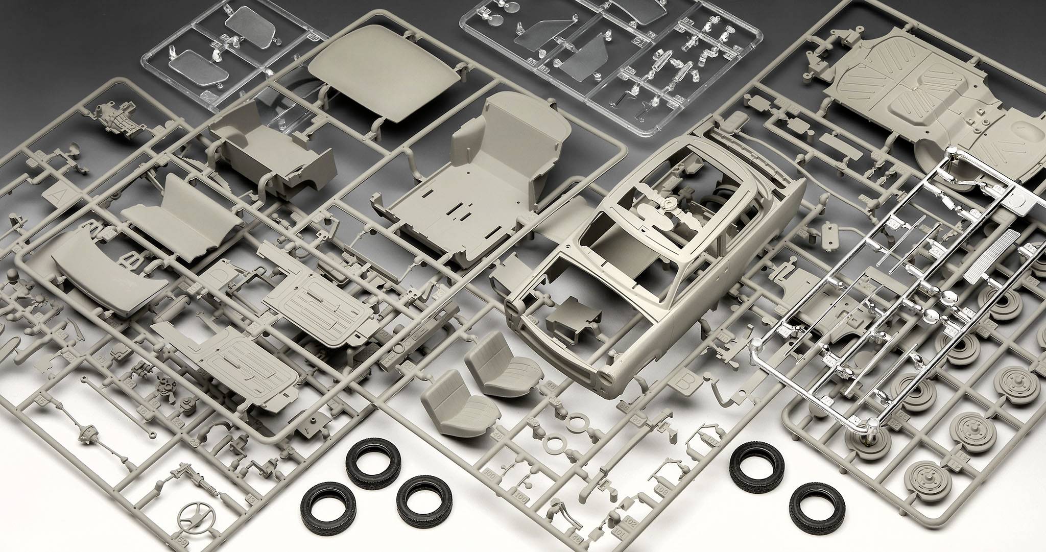 Several plastic frames with parts of a model car kit, including bodywork, seats, and tyres, spread out on a flat surface.