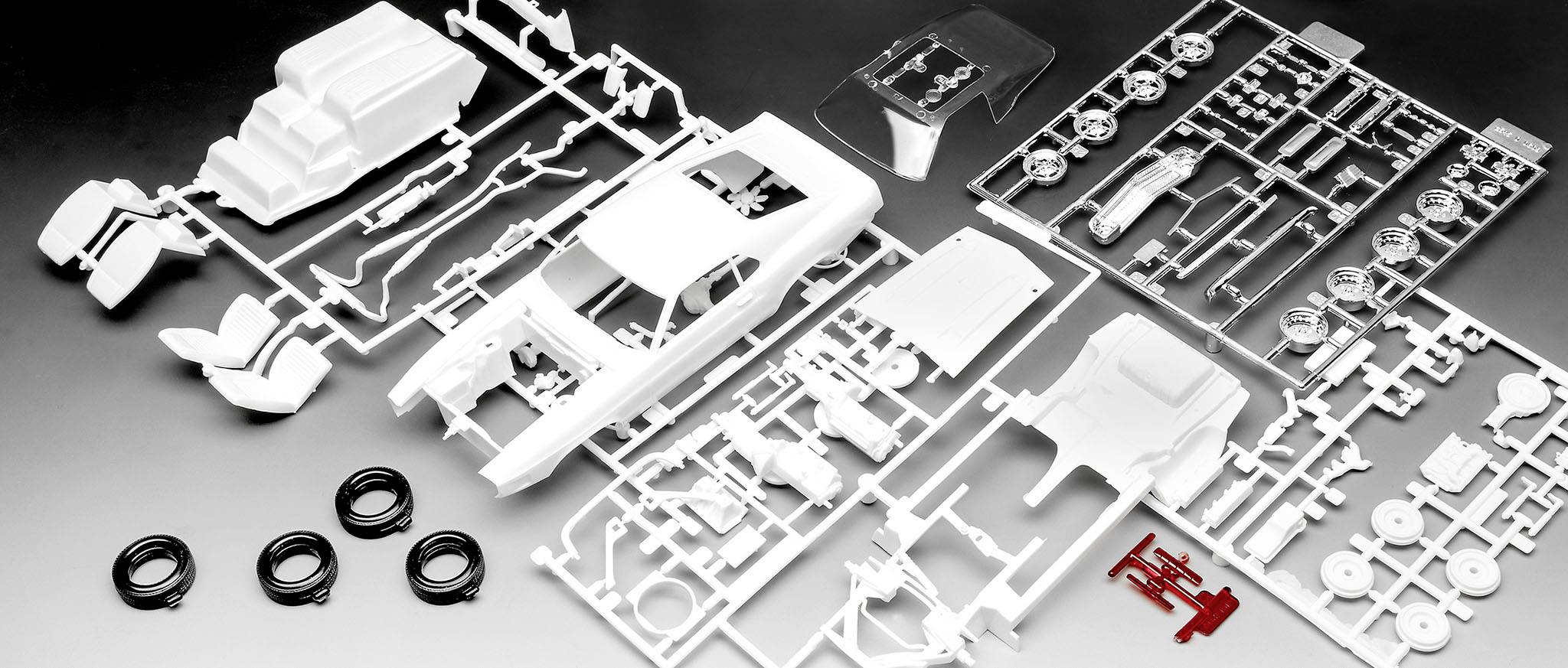 Kit for a model car, consisting of various white plastic parts, including bodywork, seats and tyres, against a dark background.