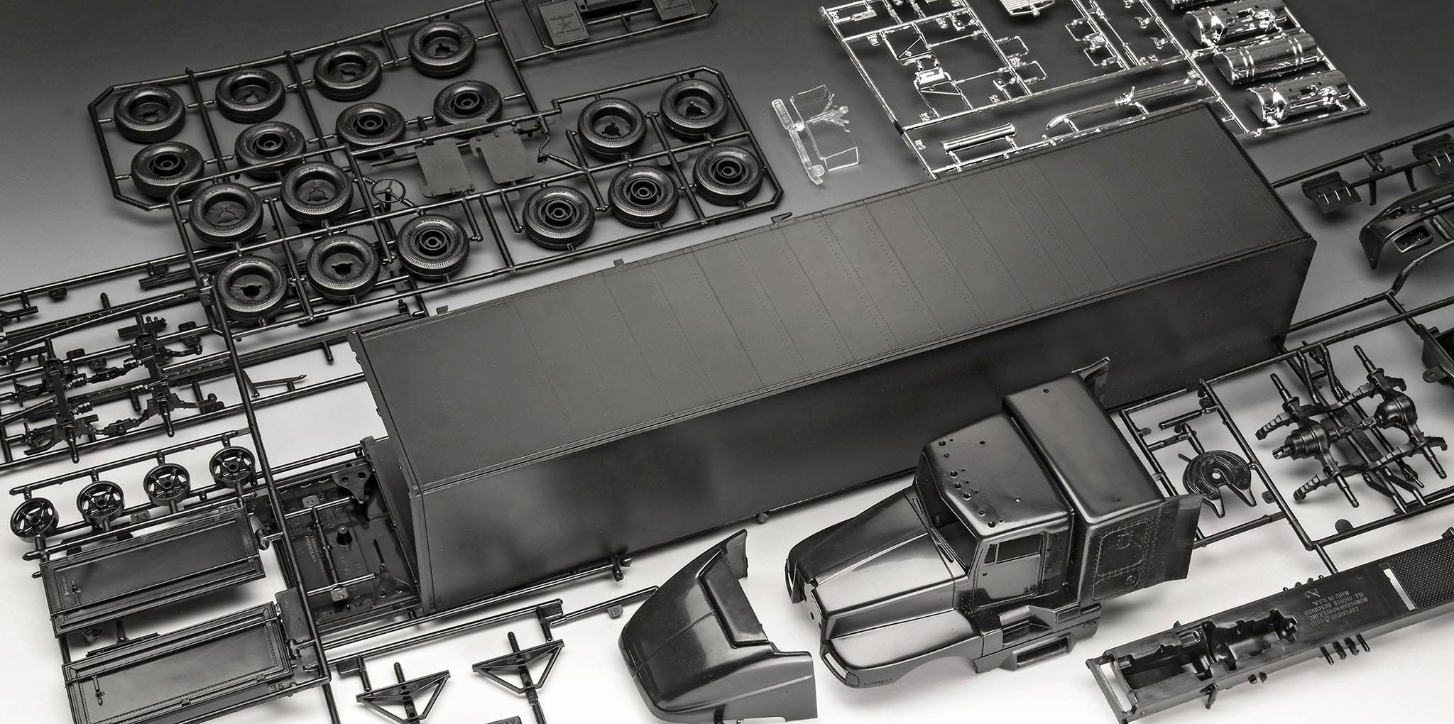 An unassembled black model kit of a lorry, consisting of multiple plastic parts and components fixed to sprues.