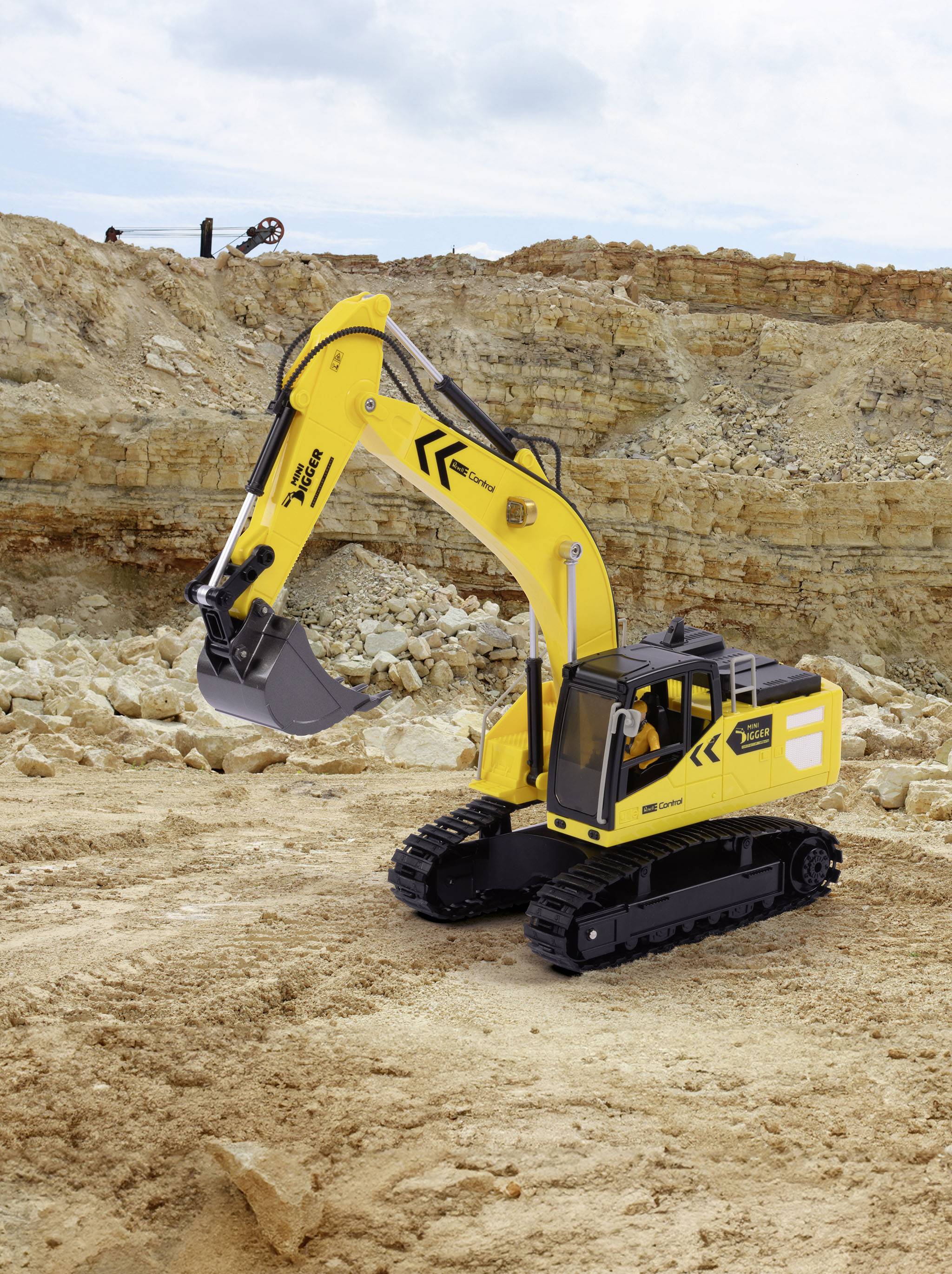 A yellow excavator with a black chassis is working in a quarry, surrounded by rocks and earth.