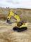 A yellow excavator with a black chassis is working in a quarry, surrounded by rocks and earth.