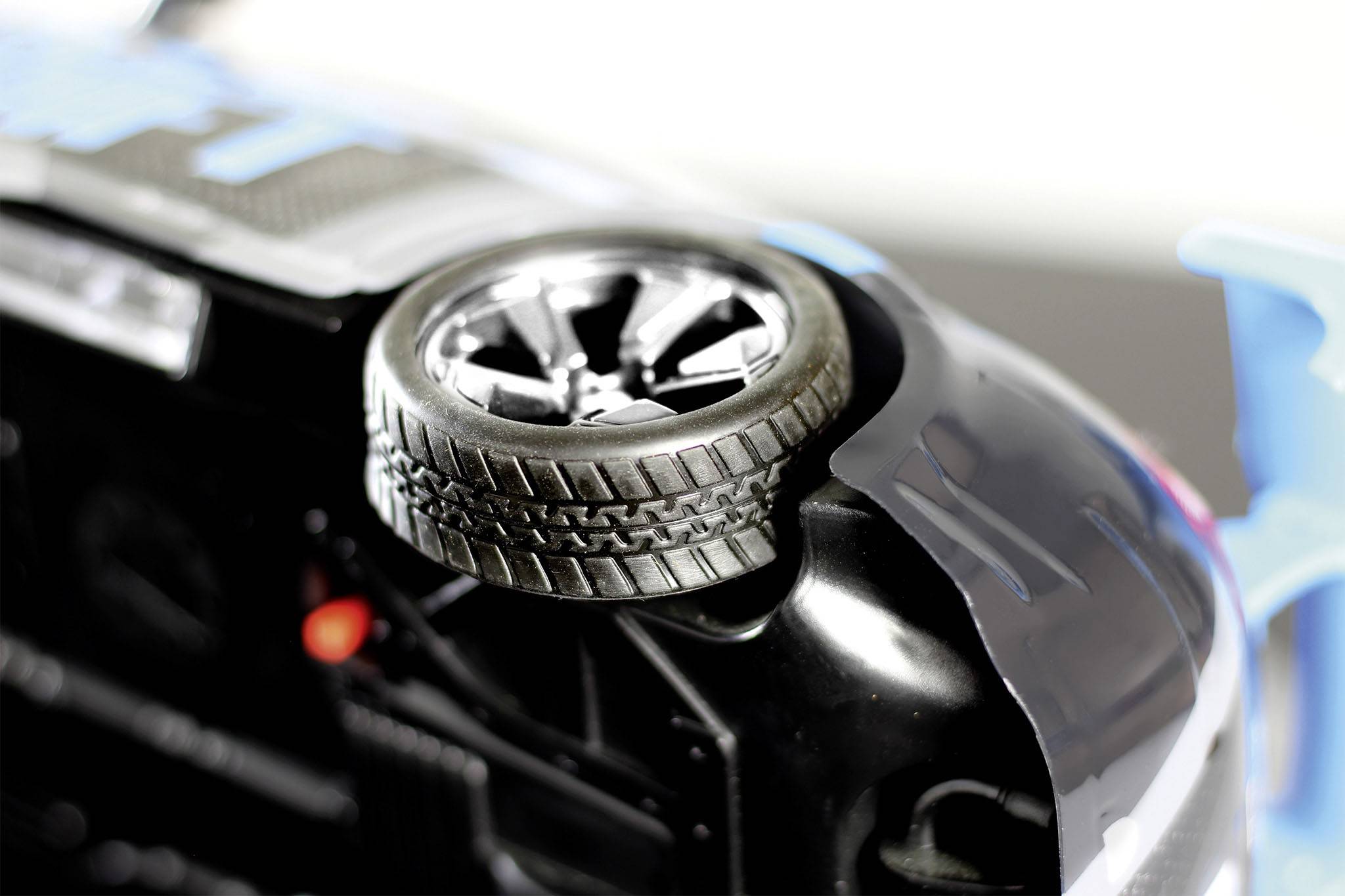 A toy car is lying on its roof, showing its tyres and underside. The surface is glossy with blue details.