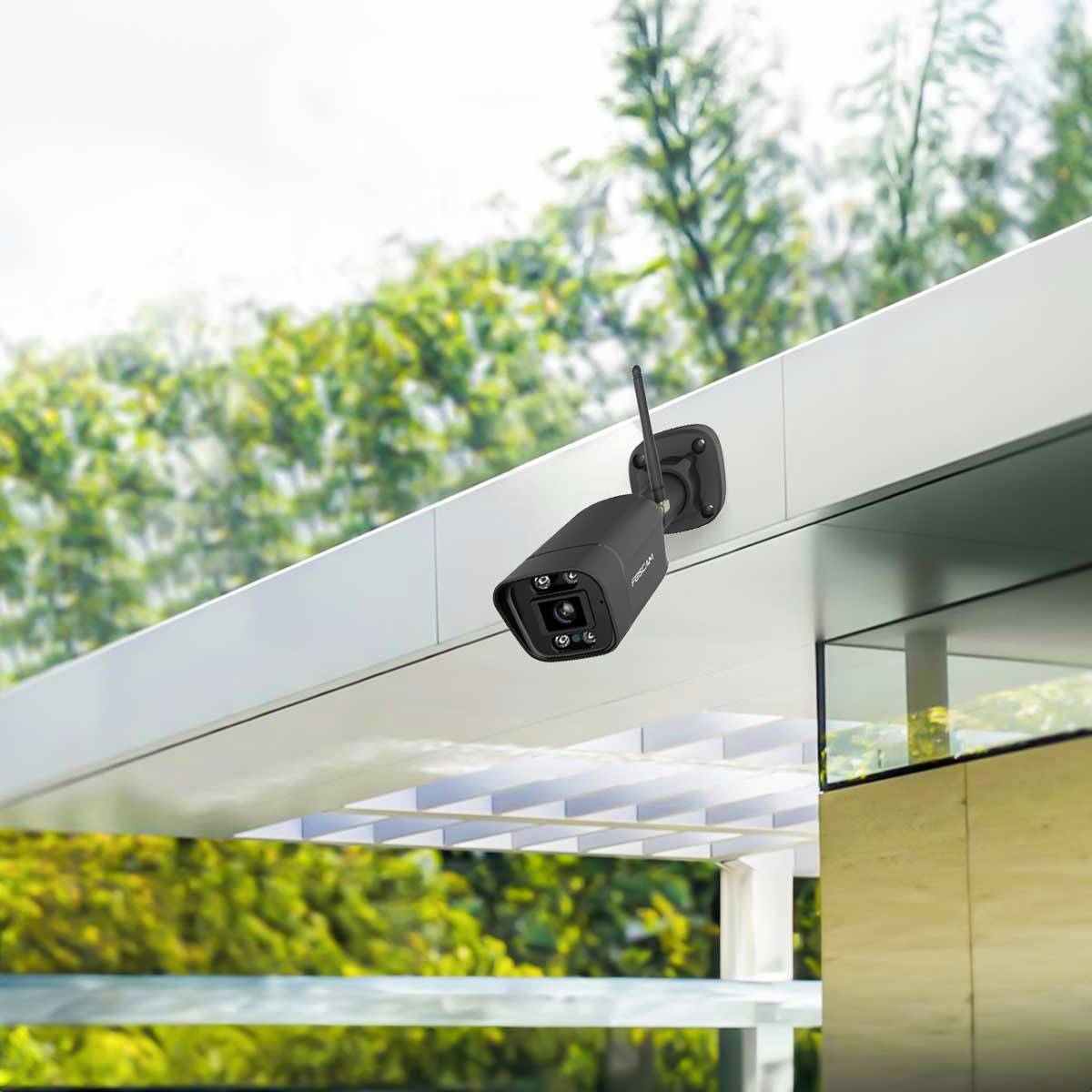 Security camera mounted on the exterior wall of a modern structure, pointing towards the surrounding partially wooded area.