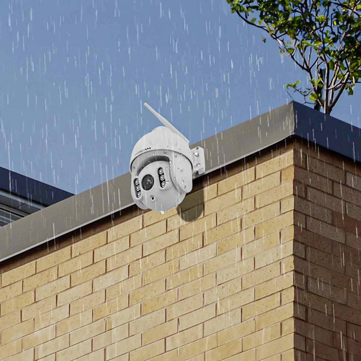A security camera is mounted on a brick wall outdoors and is recording during a rainstorm.