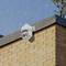 A security camera is mounted on the exterior of a brick building while it is raining.