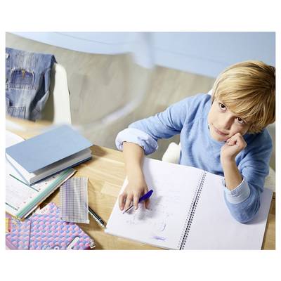 Boy sits at a desk with notebooks and pencils, writing in an open spiral notebook while looking thoughtfully upward.