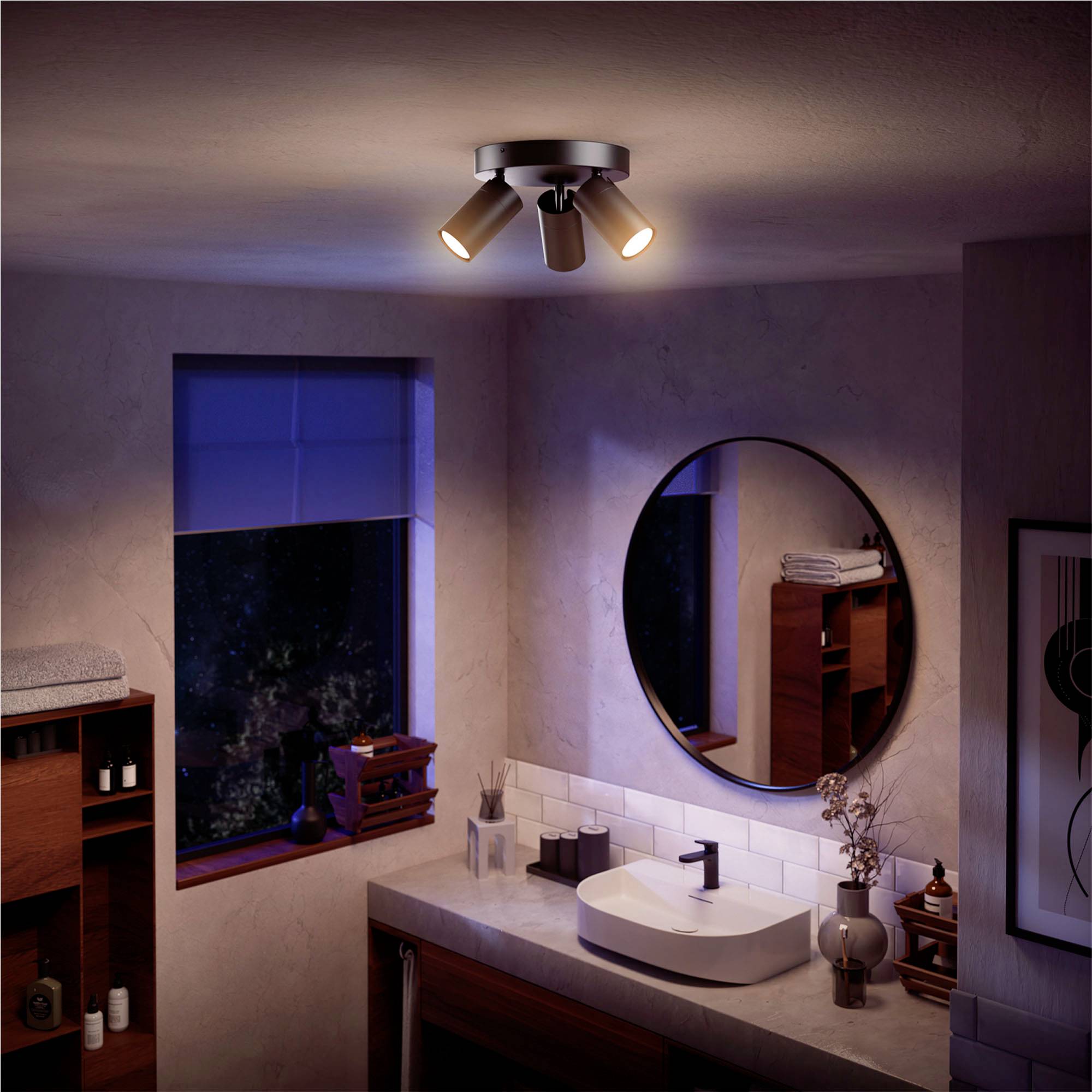 A bathroom with a bright ceiling spotlight, a round mirror above a rectangular washbasin, with decorative objects alongside.