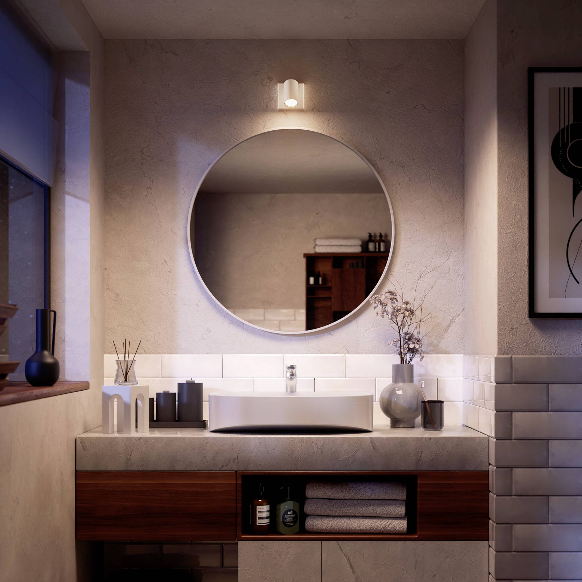 A modern bathroom fitted with a round mirror above a ceramic washbasin, flanked by decorative objects.