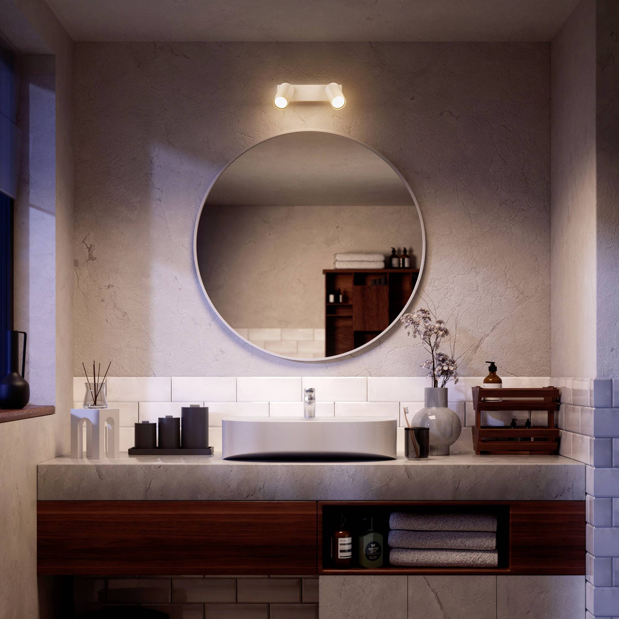 The image depicts a modern bathroom with a round mirror, a sink, and stylish shelving, atmospherically lit.