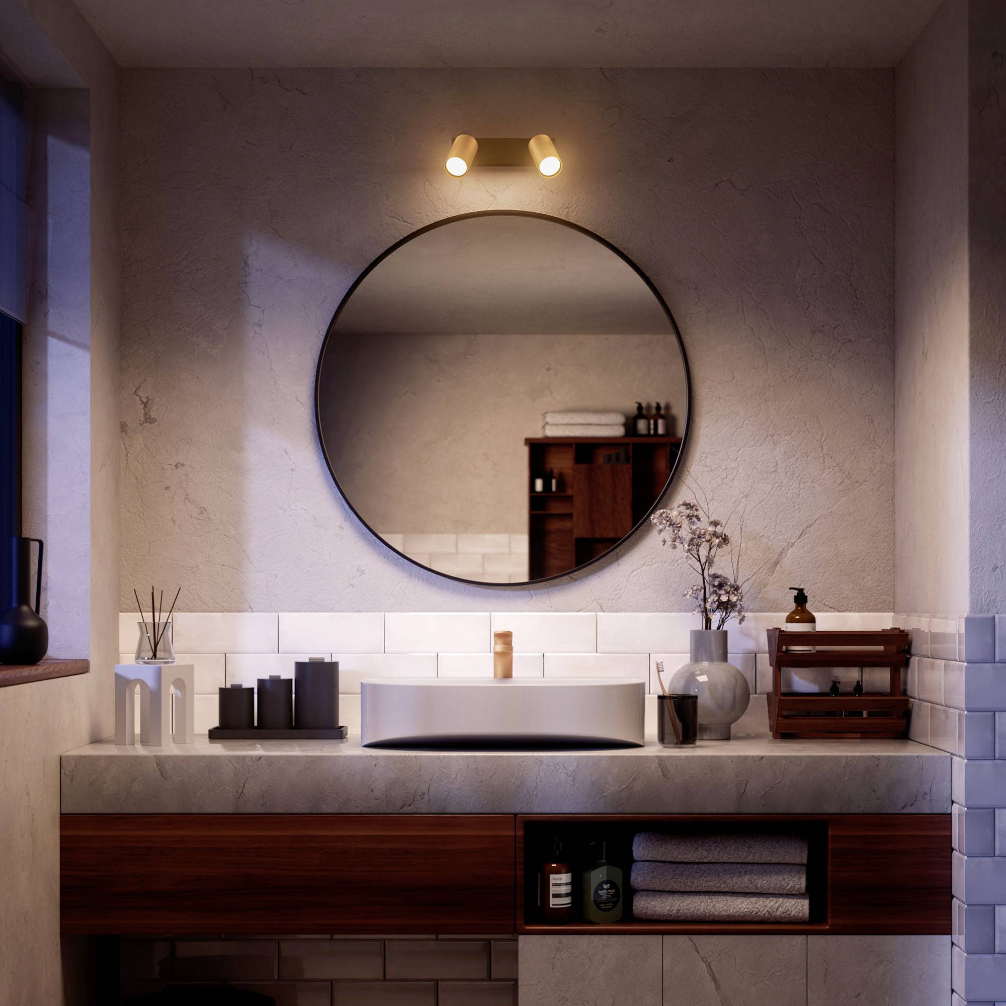 Modern bathroom with a round mirror, illuminated by wall lights. Sink on a wooden unit, decorations and towels on the shelf.