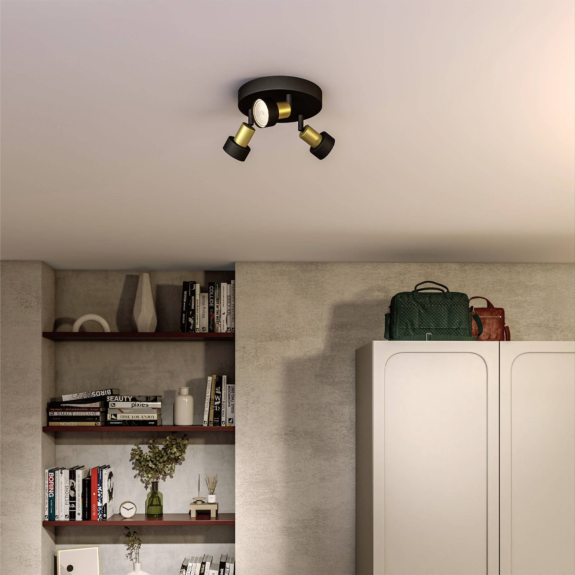 Modern living room ceiling with a three-armed spotlight. In the background, a bookshelf and white cupboards with a green and red bag.