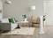 A modern living room with a grey sofa, green cushion, white coffee table, wooden table lamp and a white pedestal fan on the right.