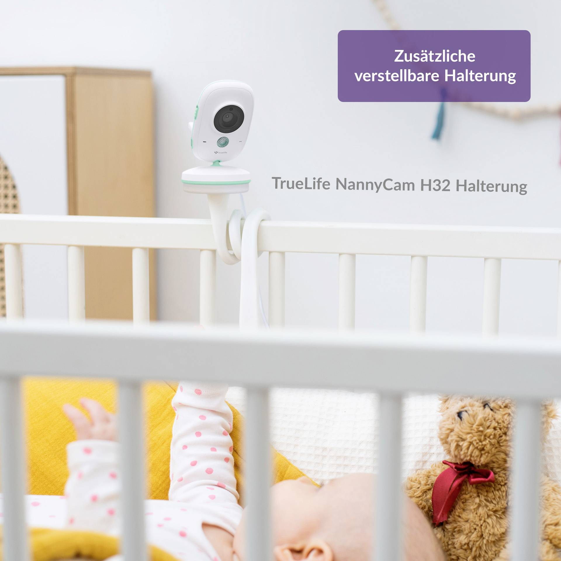 A baby monitor with an adjustable mount is attached to a cot. A baby is lying in the bed, partially obscured by a blanket and soft toy.