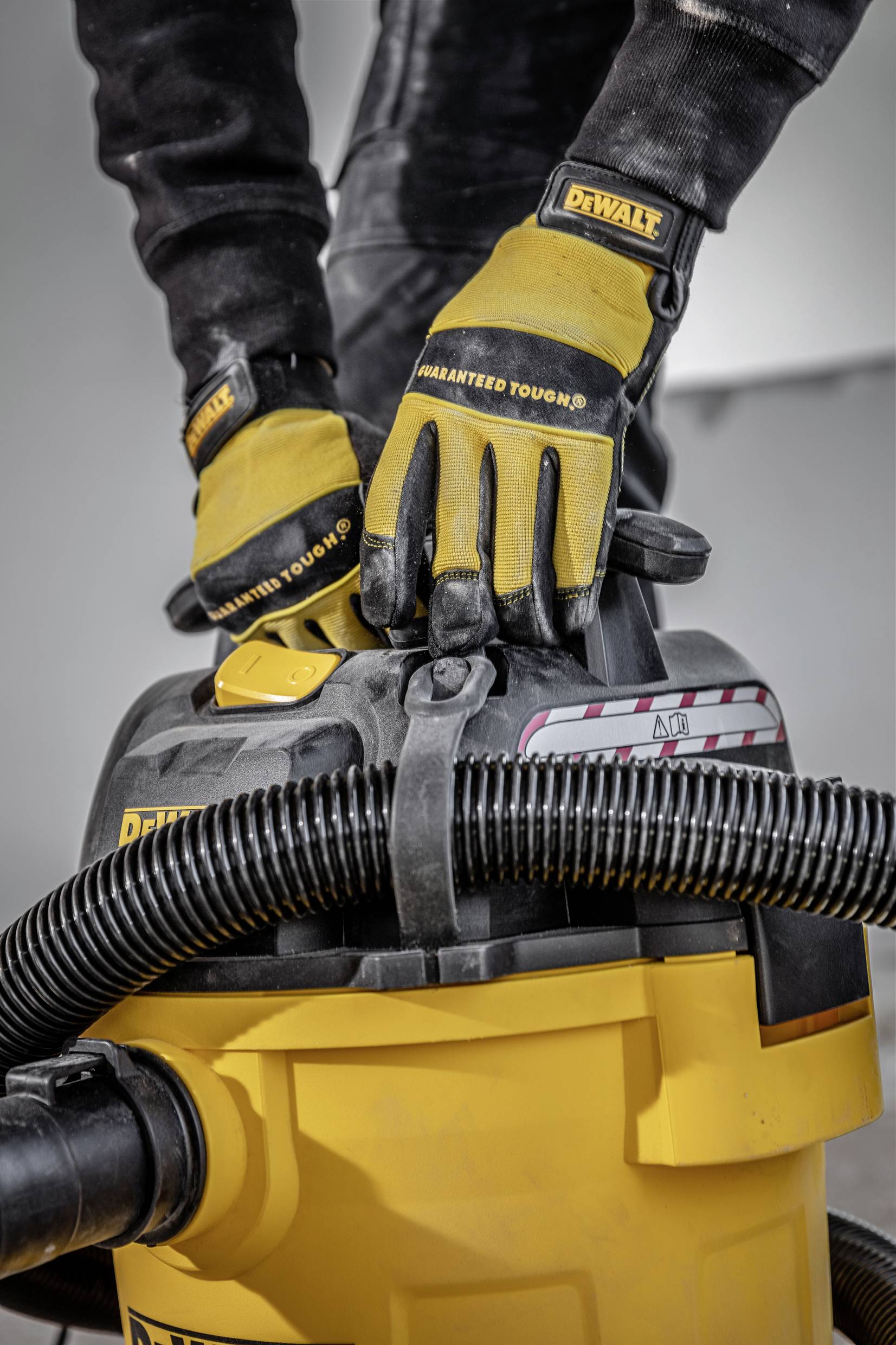 A person is operating a yellow industrial vacuum cleaner. They are wearing black clothing and yellow gloves.