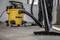 A person is using a yellow industrial vacuum cleaner on a construction site floor. Dust and dirt are being removed.