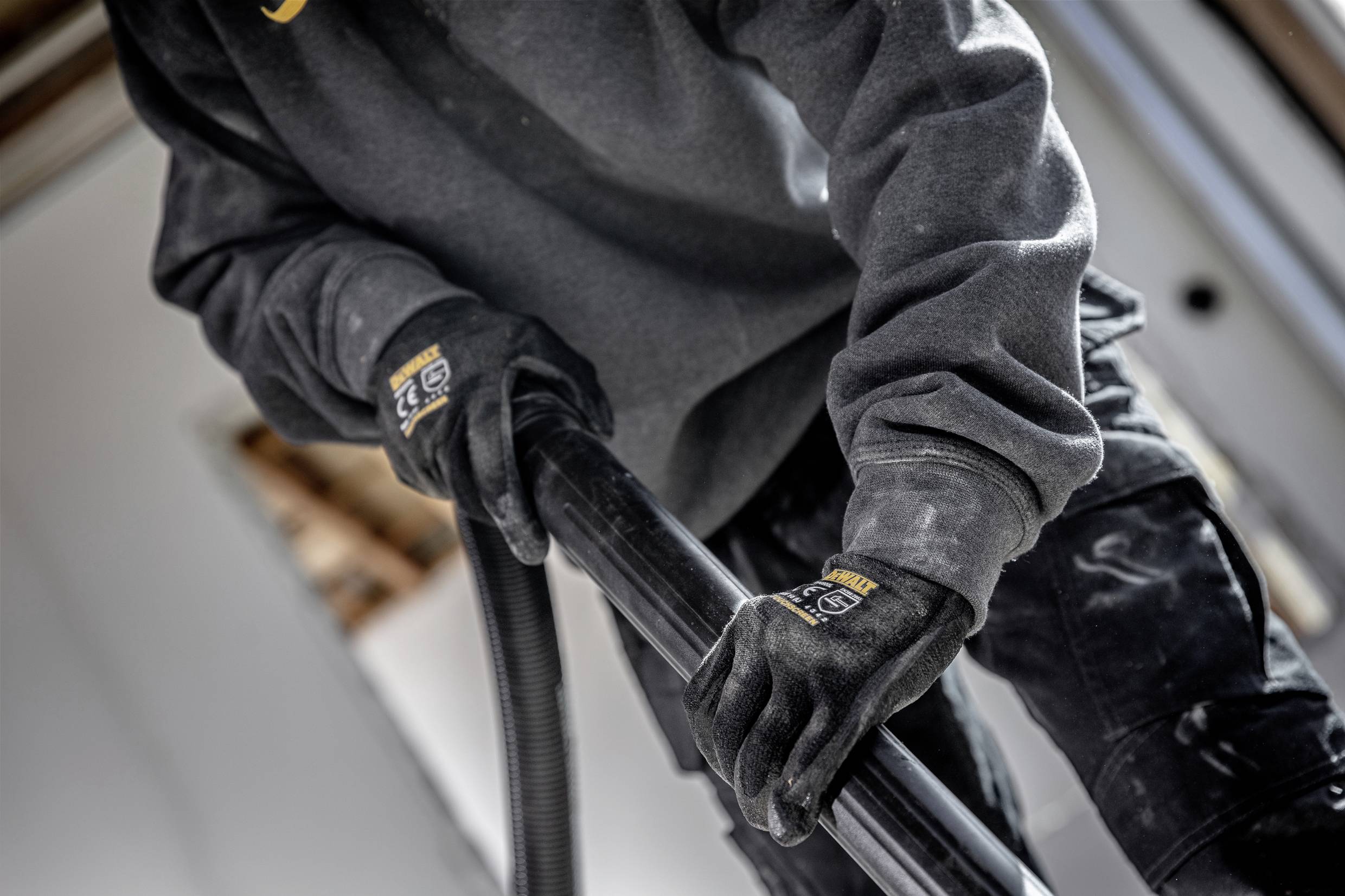 A person in workwear is holding a large hose, potentially during a construction or cleaning task.