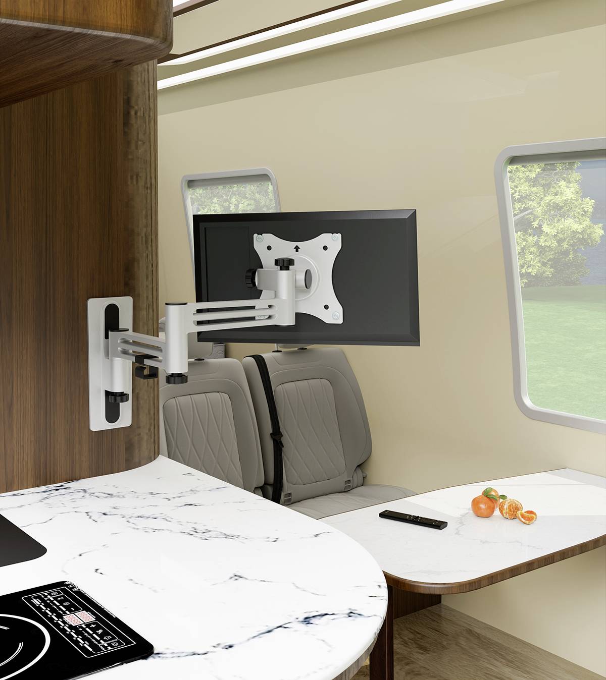 Adjustable TV mount fixed to a motorhome wall, displaying a screen, with a seating area and table nearby, and a green landscape visible outside.
