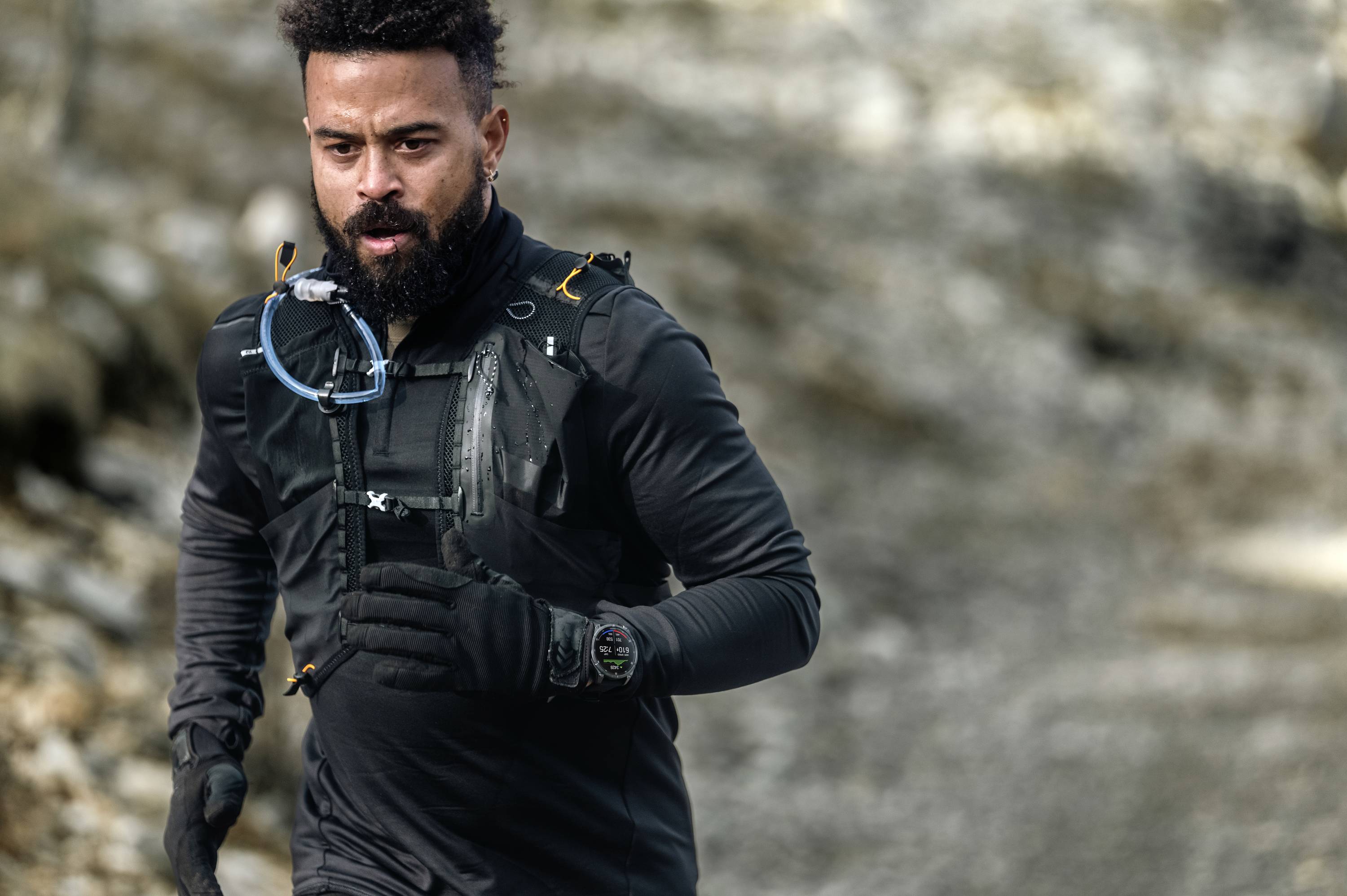 A man is jogging along a rocky path, wearing black sportswear and a watch.