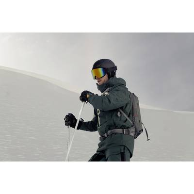 A person in ski gear is skiing down a snow-covered slope, wearing a dark green outfit, helmet, and reflective ski goggles.