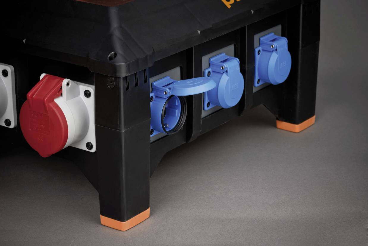 A black electrical distribution box with red and blue sockets, a blue cap open. Background in grey.