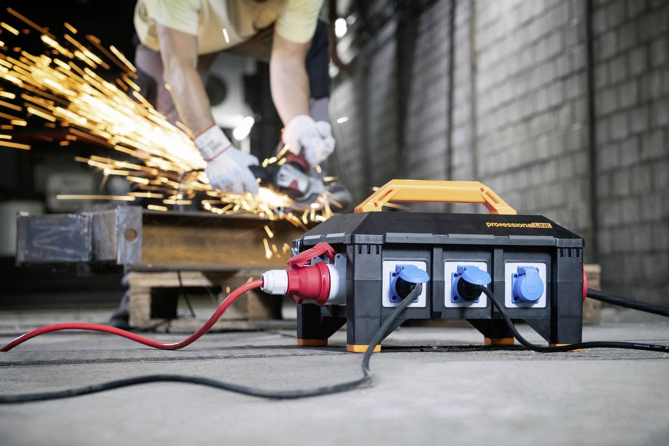 A person is grinding metal with an angle grinder. A power strip is in the foreground. Sparks are flying around.