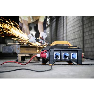 A tradesman cuts metal with an angle grinder, with sparks flying. A power distribution unit stands in the foreground.