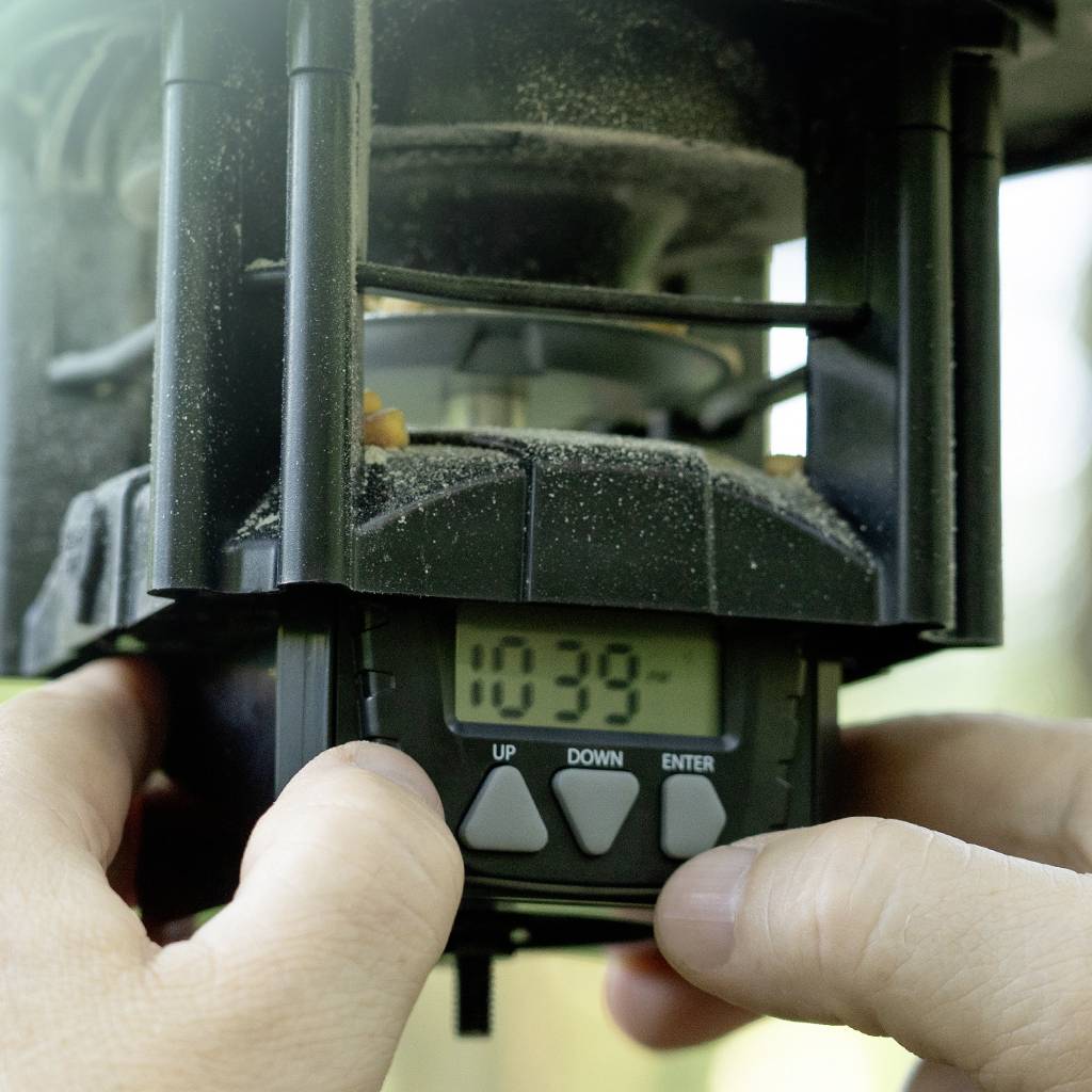 A person is setting the time on a digital timer. The display shows '10:39'. Hands are holding the timer.