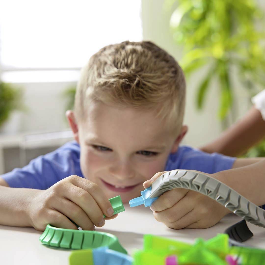 A child plays intently with colourful building blocks on a table, smiling and deeply absorbed in the activity.