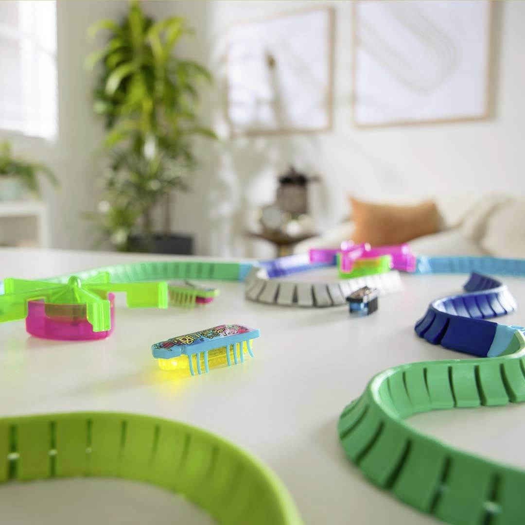 Toy cars on colourful tracks in a bright room with plants and cushions in the background.