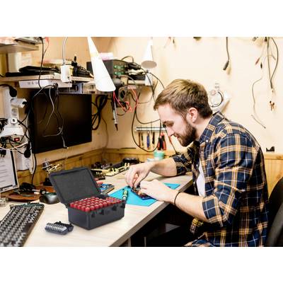 A person is working attentively on electronic components at a table in an electronics laboratory. An open toolbox is in the foreground.