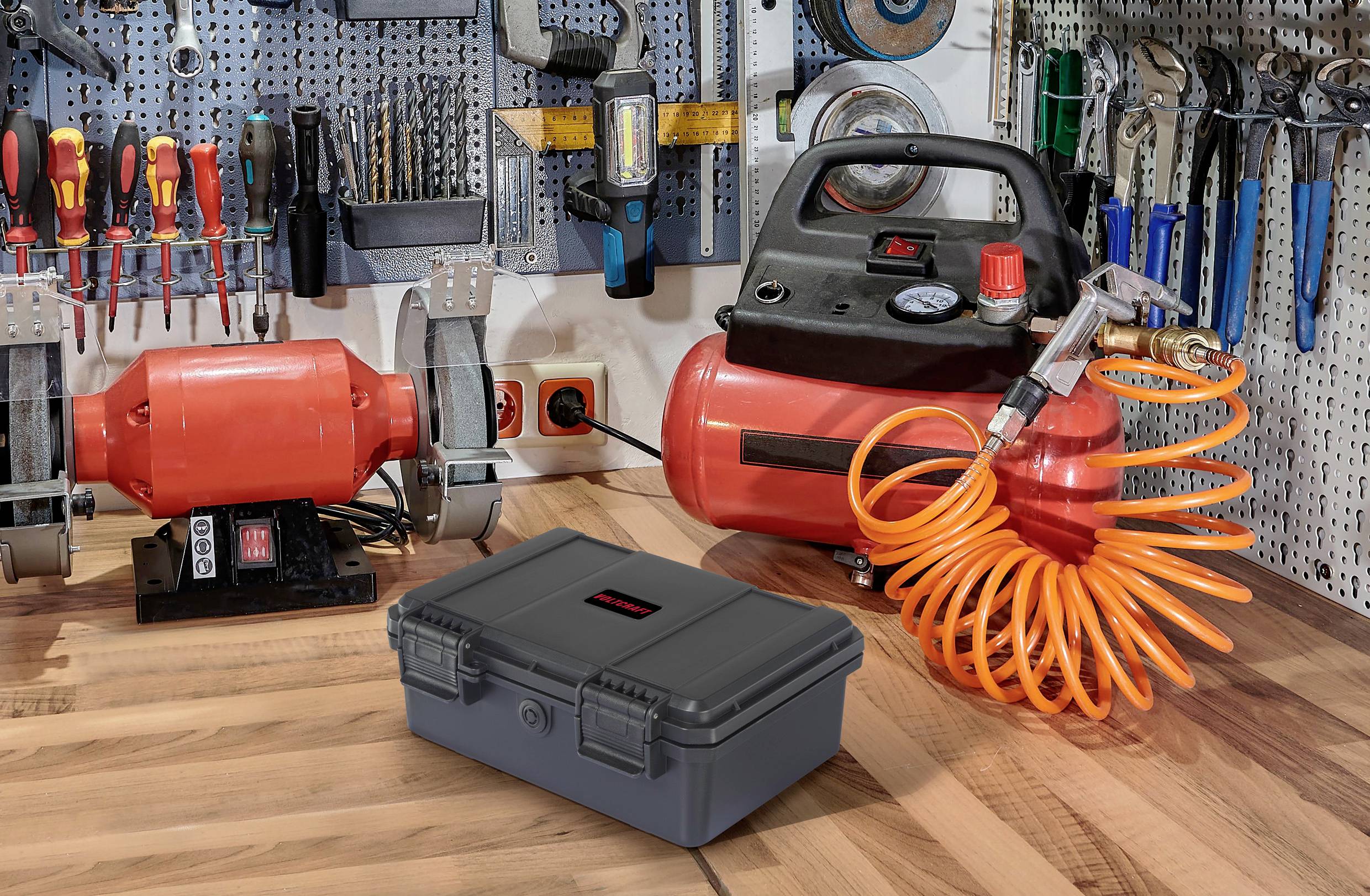 Workshop with tools on the wall, a red grinding machine, an air compressor with an orange hose, and a grey box on a wooden table.