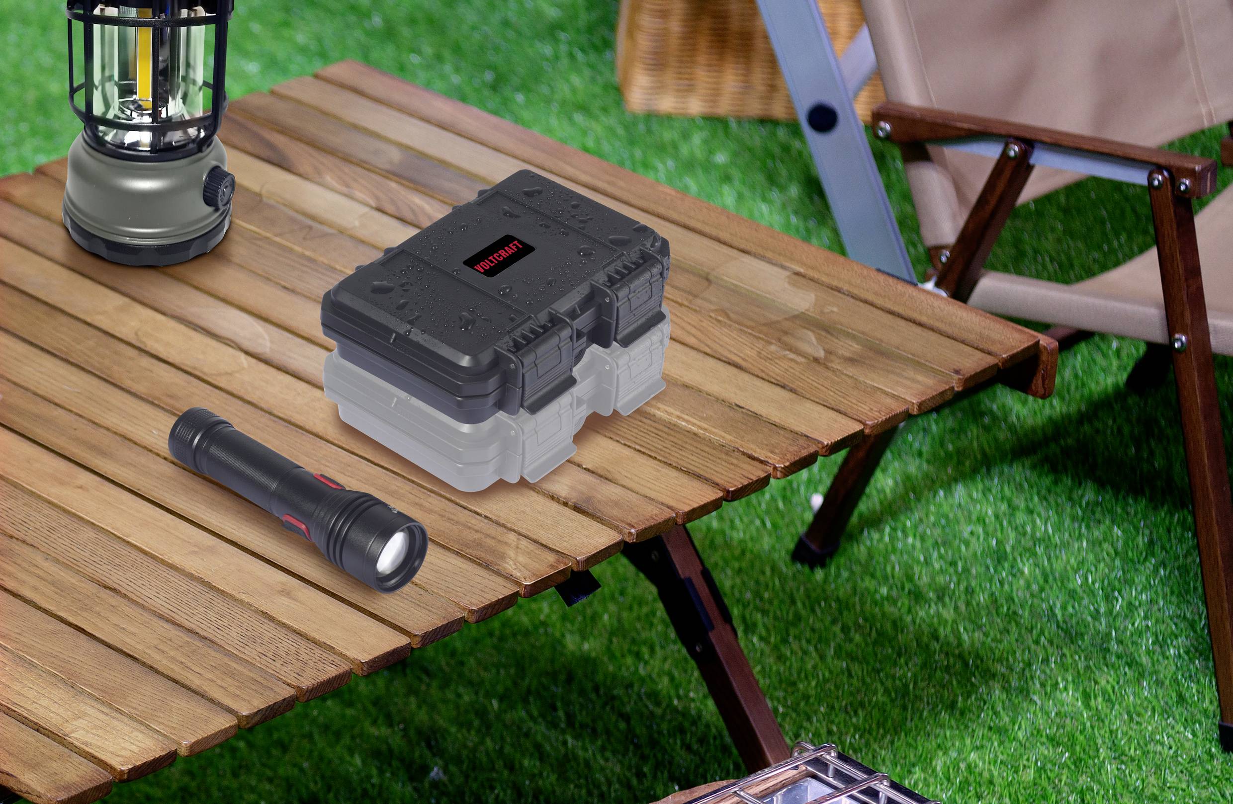 Camping scene with a folding wooden table, on which a black toolbox, a torch, and a lantern are placed. A chair is visible in the background.