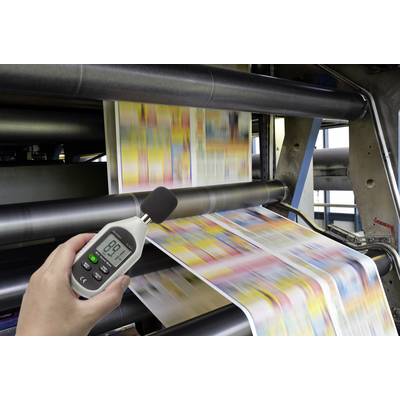 Printing press in action with focus on a hand holding a decibel meter displaying 89.1 decibels.