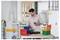 A man in a workshop organizing various colorful storage bins on a table, with tools and shelving in the background.