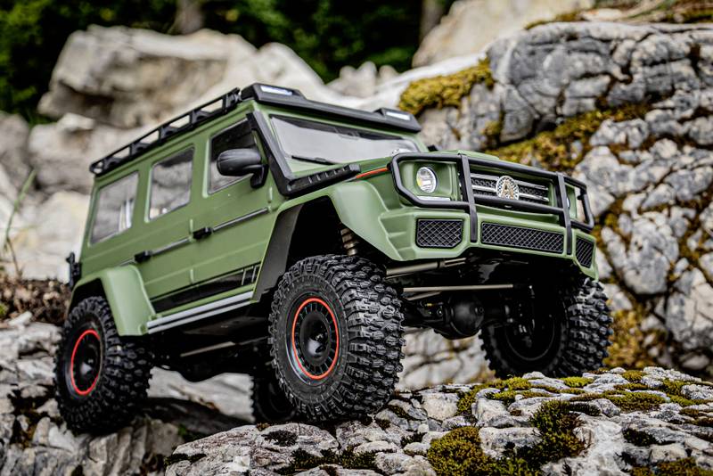 A detailed model of a green off-road vehicle drives over rocky terrain, surrounded by natural rock formations and moss.