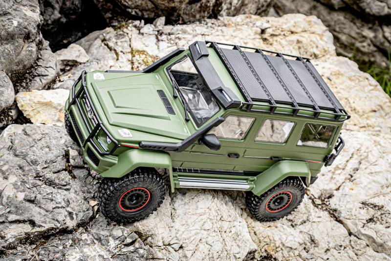 A green remote-controlled off-road vehicle model stands on a rocky surface, showcasing detail precision and robustness.