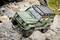 RC model car with a robust, all-terrain design, driving over rocky terrain. Vehicle is styled in olive green with a roof rack.