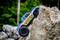 A blue model car with the number '112' climbs up a large boulder. Blurry trees can be seen in the background.