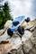 A remote-controlled car climbs a rocky surface. Trees and a cloudy sky can be seen in the background.