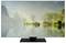 A television shows a tranquil lakeside with trees and a small cottage, surrounded by green hills under a misty sky.