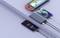 Four electronic devices are lying on a table: a portable games console, two mobile phones, and a power bank charging three devices.