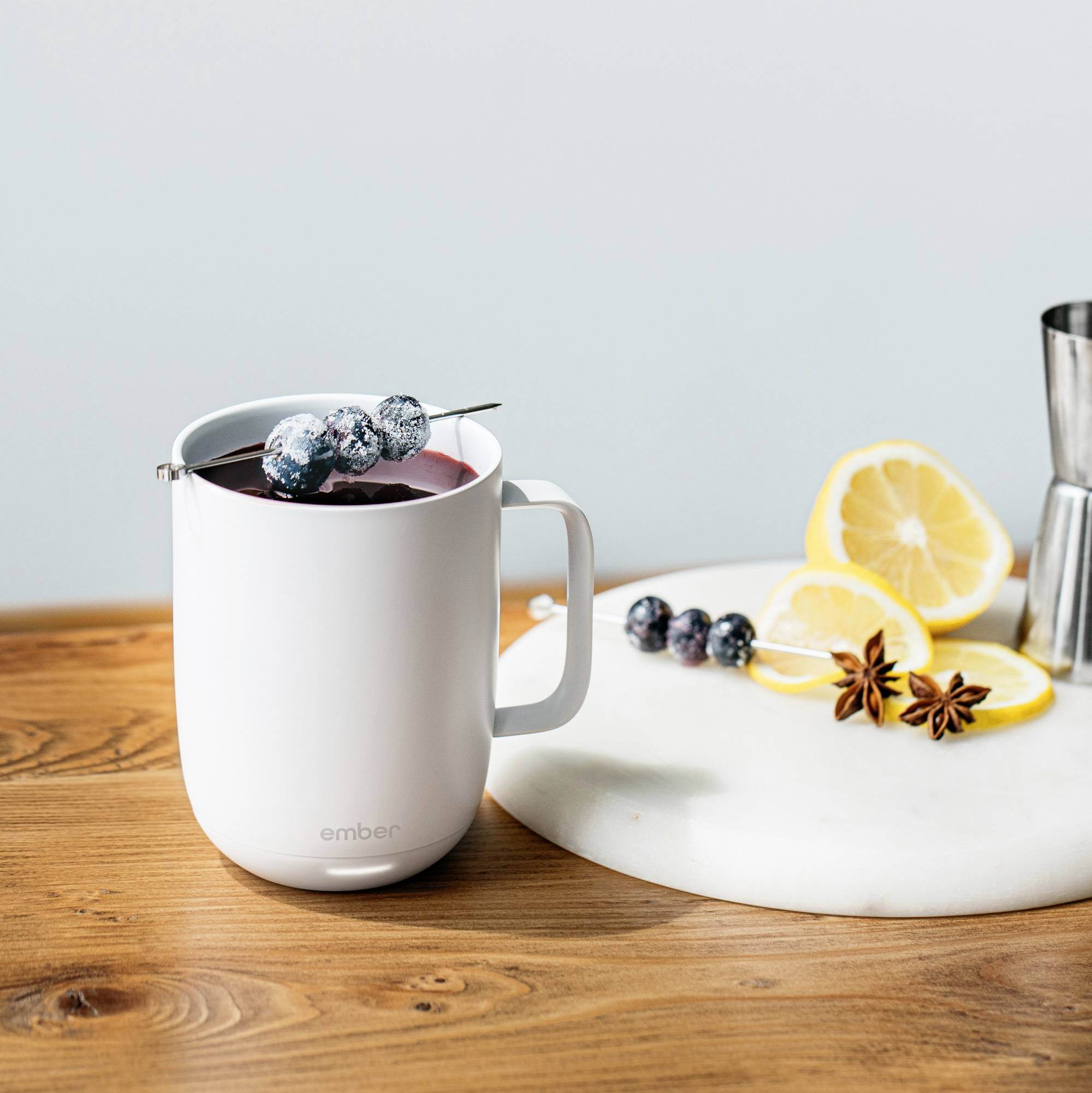 A cup with a hot beverage and blueberries on top. Beside it, a plate with lemon slices and star anise on a wooden table.