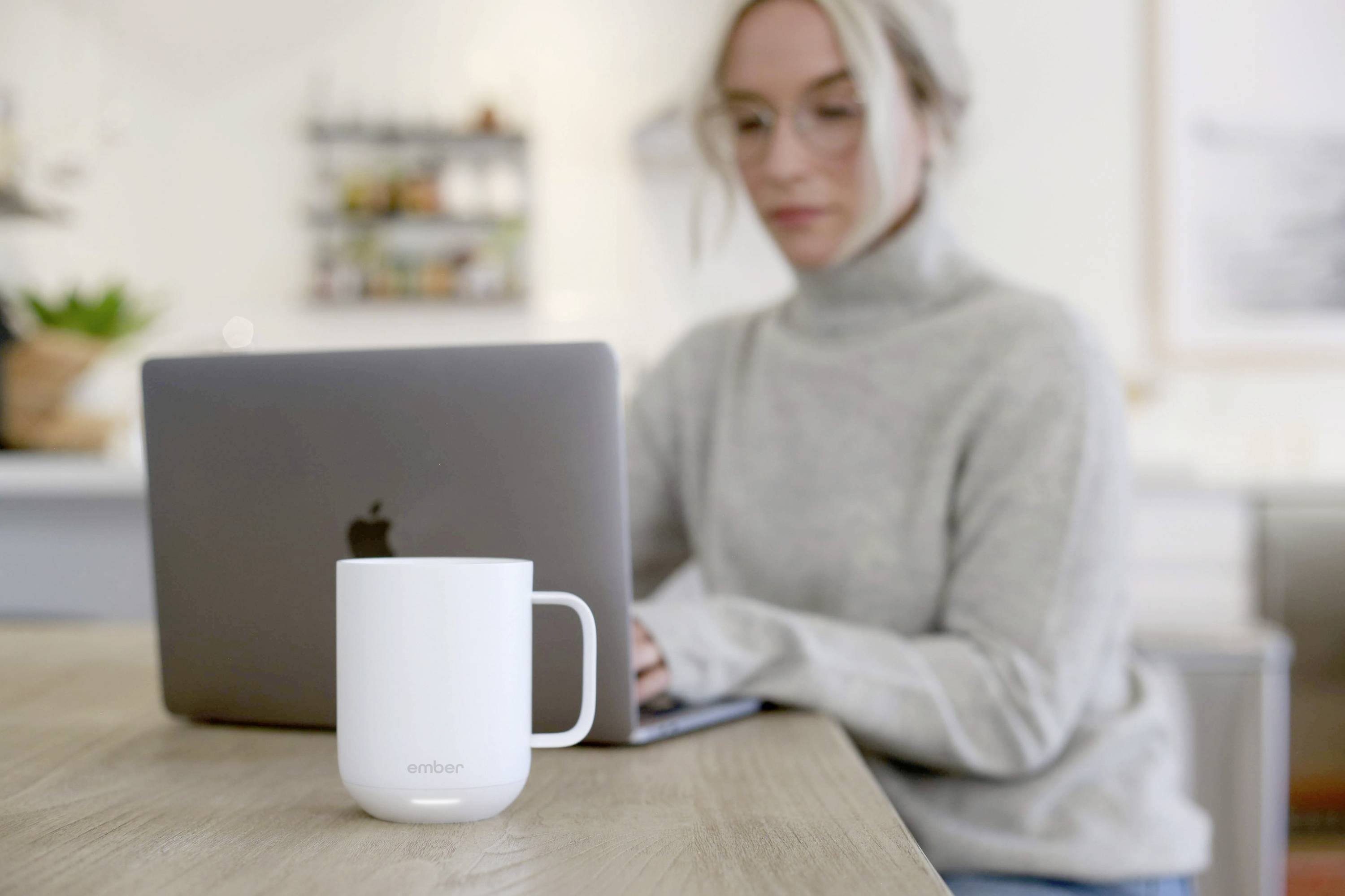 A person is concentrating intently on a laptop. In the foreground, a mug sits on a wooden table.