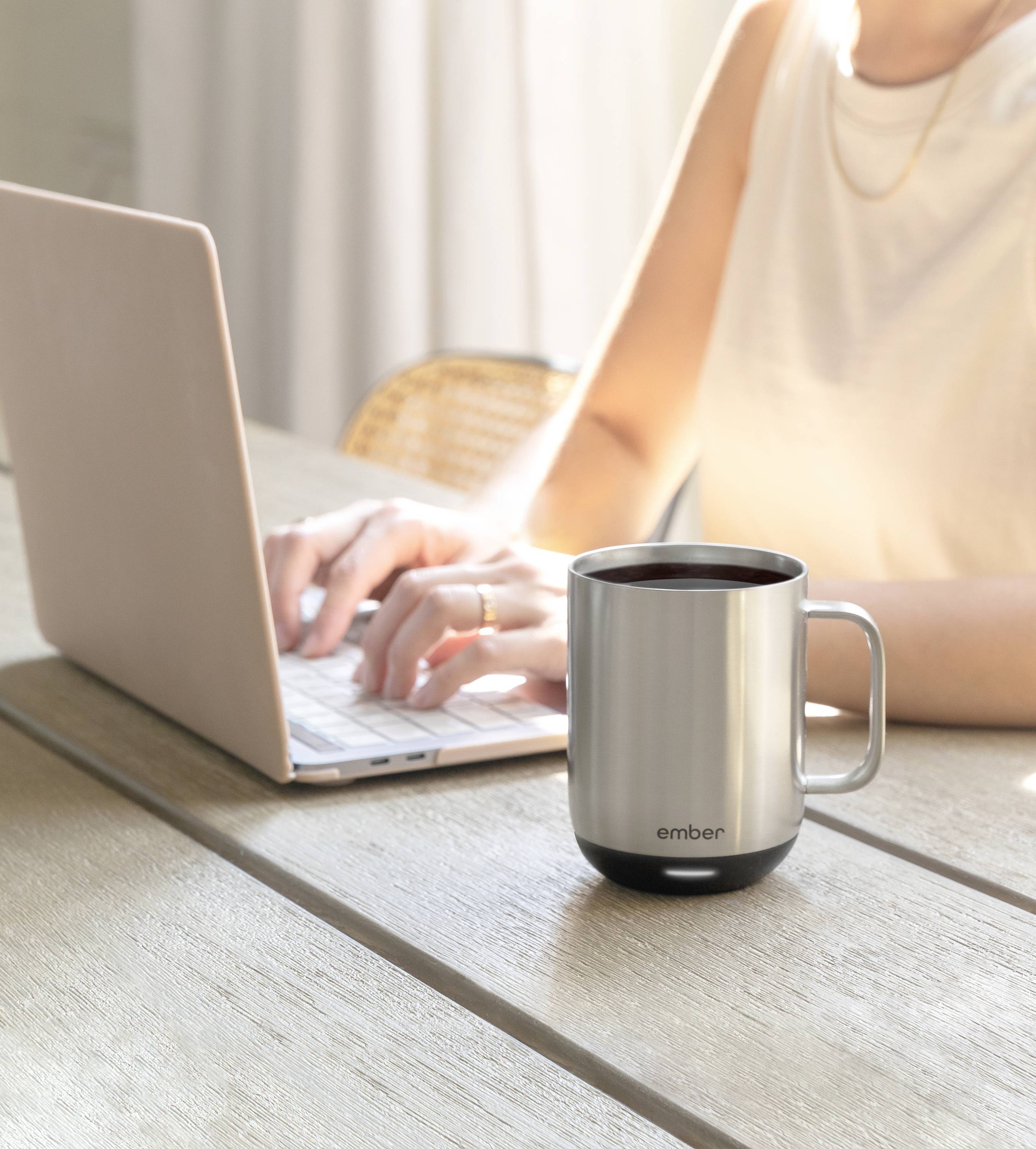 A person is typing on a laptop at a table, next to a silver thermal mug.